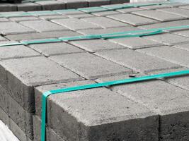 Concrete pavement blocks are arranged in neat stacks, secured with plastic straps, awaiting use in a construction project under clear skies photo