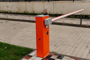 The bright orange barrier arm is installed at a parking lot entrance, designed to manage vehicle entry and enhance security during the daytime photo