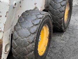 The heavy-duty tires of a bobcat are covered in mud, highlighting their use in a construction environment. The ground is gravelly and worn from activity throughout the day photo
