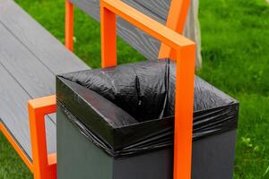 A modern bench featuring a built-in garbage container with a black liner sits on lush green grass, showcasing an aesthetic approach to waste management in public spaces photo