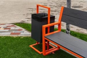 A contemporary garbage container is mounted alongside a park bench, offering a practical solution for waste disposal in a well-maintained green space photo