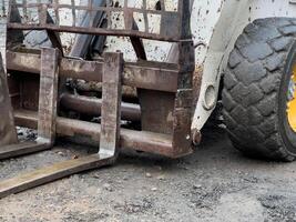 The small loader is positioned on a gravel surface, ready to engage in excavation activities, with its forks visible photo