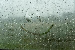 A cheerful smile is playfully etched on a fogged-up window, as rain taps against the glass, transforming an ordinary day into a moment of delight photo
