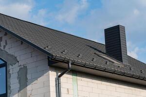 The new house features a contemporary tiled roof with a sleek design, complemented by a prominent chimney. The structure showcases a blend of modern architecture and traditional roofing photo