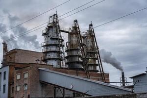 Thick, dark smoke ascends from the high smokestacks of an industrial complex, surrounded by overcast skies and powered machinery, showing signs of activity photo