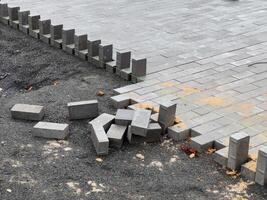 A crew is laying down paving stones to repair a section of pavement. The stones are gray and rectangular, and they are being laid in a pattern. The area around the stones is covered in gravel photo