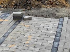 A section of pavement being repaired with gray paving stones. There are a few stones that have been laid in a row, but most of the area is still bare photo