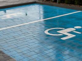 A designated parking space for disabled individuals features a blue pavement with a white wheelchair symbol clearly marked. This ensures accessibility and convenience photo