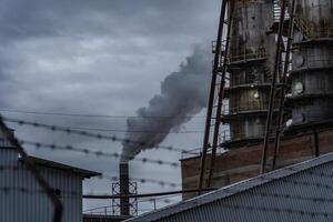 The factory features a tall structure with a brick exterior and rusted supports, releasing dense smoke into the overcast atmosphere, reflecting industrial activity photo