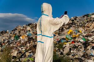 Dressed in a protective suit, an individual examines a landfill site overflowing with waste while standing amidst the heaps of discarded materials under the sun photo