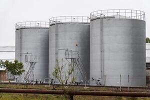Three large, gray cylindrical storage tanks are positioned next to one another, equipped with metal ladders and catwalks, indicating an industrial environment photo
