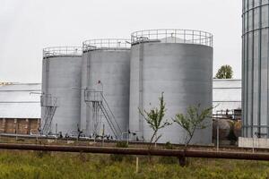 Three large gray storage tanks are situated in an industrial area, complete with metal catwalks and ladders, indicating a functional facility photo