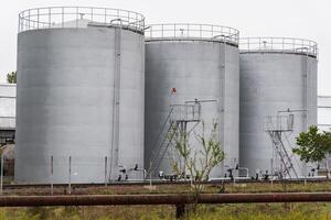 Three large gray storage tanks are positioned closely together at an industrial site. Metal catwalks and ladders provide access for maintenance and monitoring photo