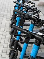 A row of blue scooters are parked on a brick sidewalk. The scooters are all facing the same direction, and they are all parked next to each other. The scene gives off a sense of order and organization photo