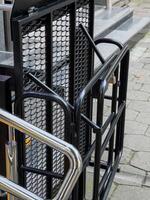 A black metal ramp is folded up, attached to the side of a building. The ramp has a metal mesh surface and a steel handrail. It is likely used to provide access to people with mobility issues photo