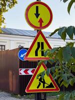 Brightly colored construction signs alert drivers to changing road conditions, including a merge and worker presence, set against a vibrant urban backdrop photo