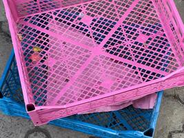 Two distinctively colored plastic crates, one pink and one blue, are stacked on the ground, surrounded by hints of a bustling marketplace atmosphere nearby photo