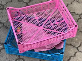 Vibrant pink and blue plastic crates are stacked on a patterned pavement, hinting at their use for storing goods at a lively market atmosphere under the warm sun photo