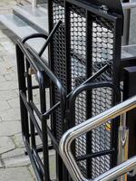 A black metal ramp with a mesh panel folds up against the side of a building, providing wheelchair access photo