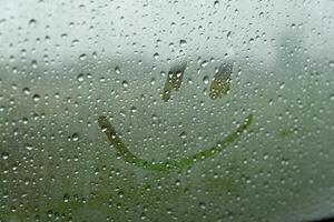 Raindrops create a dreamy backdrop as a playful smile emerges on the glass, mixing joy with the soothing sounds of a heavy downpour outside in nature photo