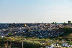 Heavy machinery works on a sprawling landfill surrounded by greenery, showcasing the scale of waste management in this rural environment during sunny weather photo