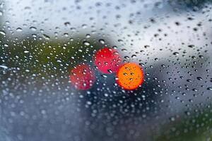 Raindrops create a textured effect on the car window, blurring bright red lights from vehicles ahead in the busy city as rain falls steadily photo
