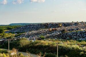 Mountains of refuse accumulate at a landfill site surrounded by greenery, highlighting the environmental impact of waste management practices under the afternoon sun photo