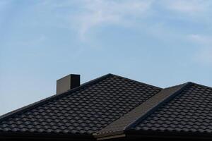 The structure features two gabled roofs with textured tiles, standing prominently under a bright blue sky, highlighting the craftsmanship of the residential architecture photo