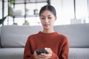 Asian Woman controlling smart home. mobile phone with smart home app in living room. touch screen ai technology. Remote control system. photo