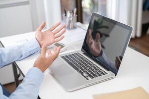 a man is gesturing while sitting at a desk with a laptop photo