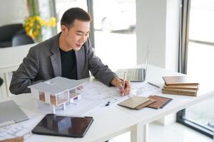 Architecture Man is working on a project with a laptop and a model of a house photo