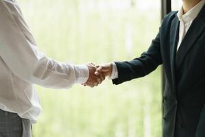 two business people shaking hands in front of a window photo