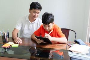 a father and a boy sitting at a table with a tablet photo