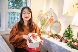 a woman holding a gift box in front of a christmas tree photo