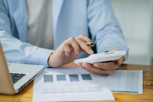 a man is using his calculator while sitting at a desk with a laptop and papers photo