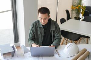Architecture man sitting at a table with a laptop and construction paper photo