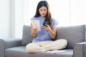 Asian woman holding paper document calculating money savings paying bills in mobile application using smart phone payment online with paying household bills managing budget photo