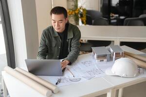 a engineer man sitting at a table with a laptop and construction plans photo