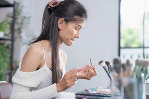 asiático mujer aplicando hacer arriba Fundación y ocultador hacer arriba en cara con productos cosméticos cambio de imagen, diario rutina foto