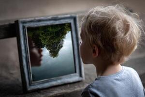A young child looking at a mirror with a reflection of a tree photo