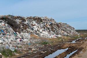 Overfilled landfill with visible garbage, plastic, waste, and debris under blue sky polluting soil, contributing to climate change. photo