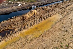 Muddy Ditch with Polluted Water and Tire Tracks Reveals Environmental Impact and Soil Disturbance in a Rural Landscape photo