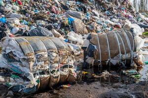 Overflowing landfill with compressed trash bundles reflects in a puddle of water showing environmental pollution issues. photo