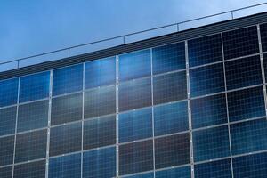Exterior shot of large solar panel array on building facade against clear blue sky, reflecting daylight and providing renewable energy photo