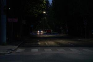 Vehicles Traveling on Illuminated Road at Twilight With Crosswalk and Trees Casting Shadows in the Night photo