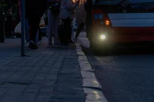 Evening Scene of People Boarding Bus at Stop with Accessibility Symbol and Paved Sidewalk Leading to the Road photo