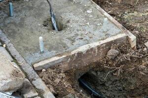Fresh concrete slab with anchor bolts set in a wooden form during construction, with ground and underground wire conduit visible photo