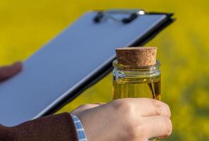 A researcher holds a jar of biofuel with a cork lid while examining data on a clipboard, surrounded by vibrant yellow field flowers, emphasizing sustainable energy photo