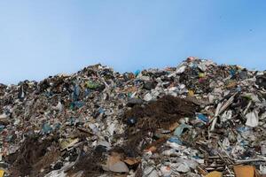Landfill Site with Large Heap of Discarded Trash and Waste Materials Against Clear Blue Sky, Showing Environmental Issues photo