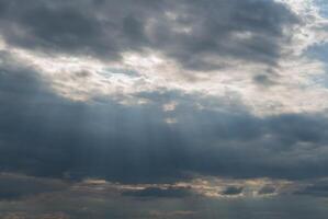 Dark clouds fill the sky, while beams of sunlight pierce through, creating a stunning contrast during the late afternoon hours in a tranquil setting photo